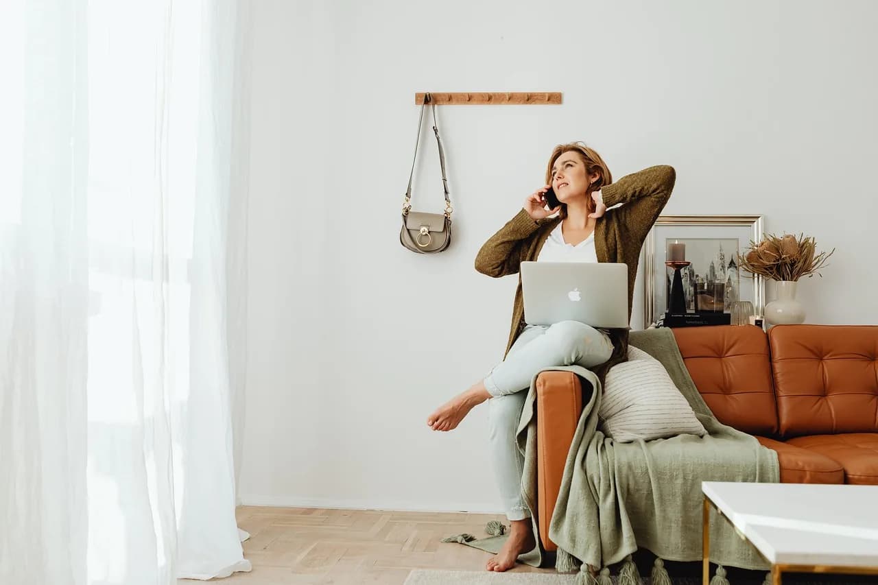 Someone with a laptop open in a bright living room, taking a call